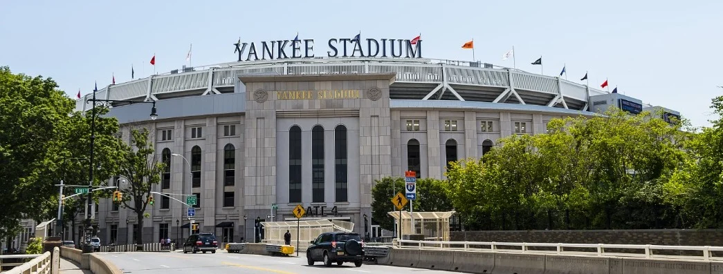 Stenen gevel met de tekst Yankee Stadium en vlaggenmasten boven de hoofdingang met verkeer op de brug ervoor