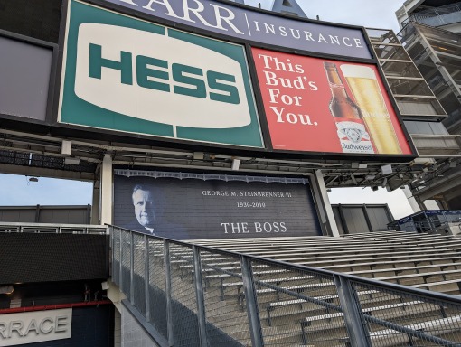 Groot digitaal scorebord met reclames en een eerbetoon aan oud eigenaar George Steinbrenner boven lege tribunes in Yankee Stadium