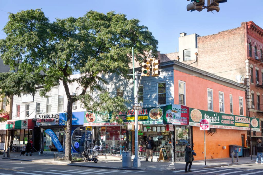 Straathoek met kleurrijke winkelpuien, een boom en voorbijgangers op Arthur Avenue in de Bronx