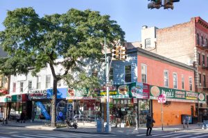 Straathoek met kleurrijke winkelpuien, een boom en voorbijgangers op Arthur Avenue in de Bronx