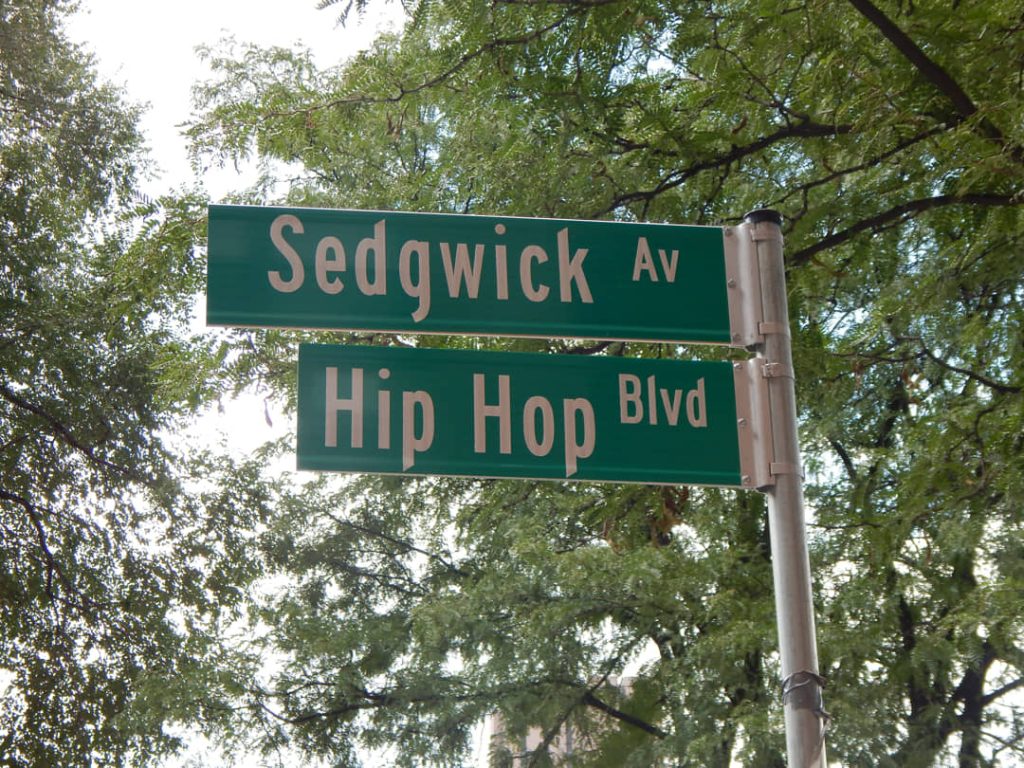 Twee groene straatnaamborden met de teksten Sedgwick Avenue en Hip Hop Boulevard tegen een achtergrond van bomen in de Bronx