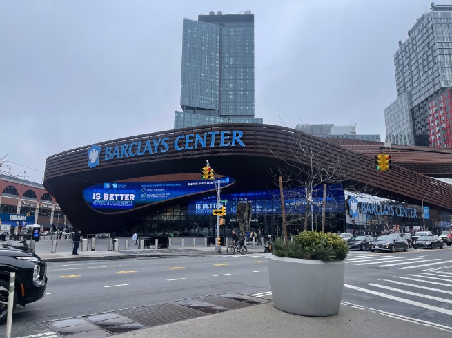 Golvende, roestbruine gevel van het Barclays Center met reclameschermen en hoge gebouwen op de achtergrond in Brooklyn