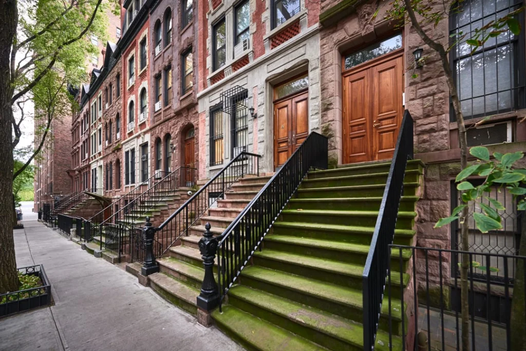 Groen bemoste stenen stoeptrap met zwarte leuning naar de houten voordeuren van bruinstenen woonhuizen in Brooklyn