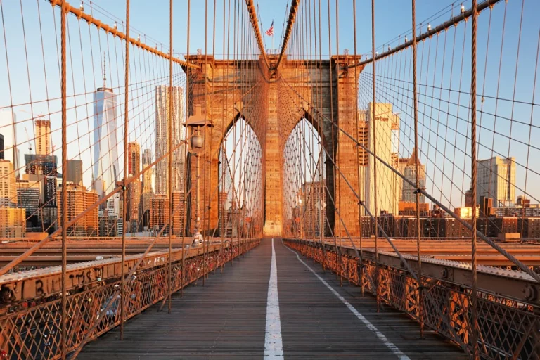 Houten loopbrug over de Brooklyn Bridge met de stenen pijler op de achtergrond, badend in warm gouden avondlicht