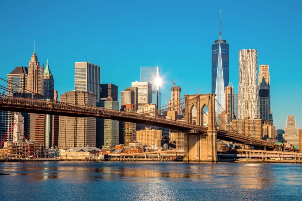 De Brooklyn Bridge over het water met op de achtergrond de wolkenkrabbers van Lower Manhattan, fel verlicht door de laagstaande zon