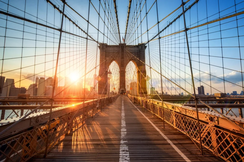 Onderaanzicht van de stenen boog en kabels van de Brooklyn Bridge met fel zonlicht dat tussen het staaldraad doorschijnt