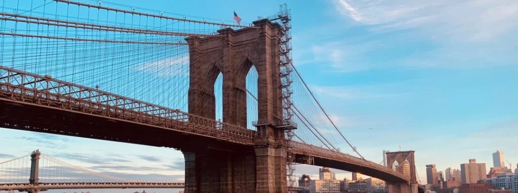Onderaanzicht van de gotische stenen pijler en kabels van de Brooklyn Bridge tegen een blauwe lucht met wolken