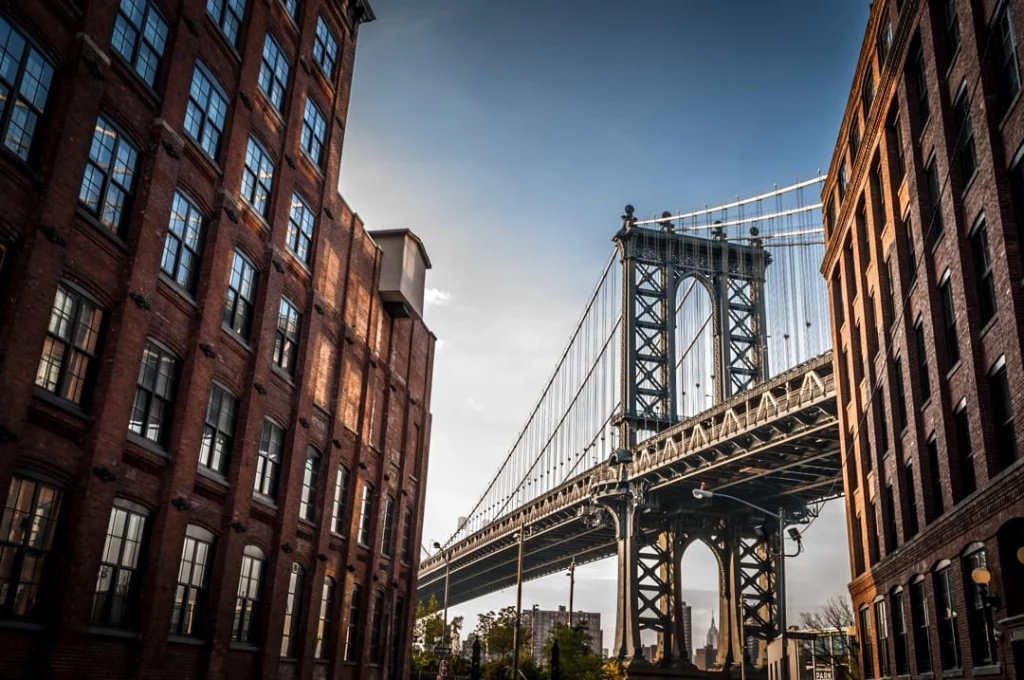 Smalle straat tussen bakstenen pakhuizen in Dumbo, Brooklyn met de Manhattan Bridge en de skyline van Manhattan zichtbaar in de verte