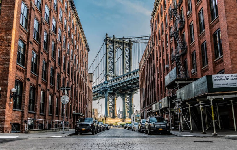Kasseienstraat tussen bakstenen pakhuizen met geparkeerde auto's, uitkomend op de Manhattan Bridge in de wijk Dumbo in Brooklyn