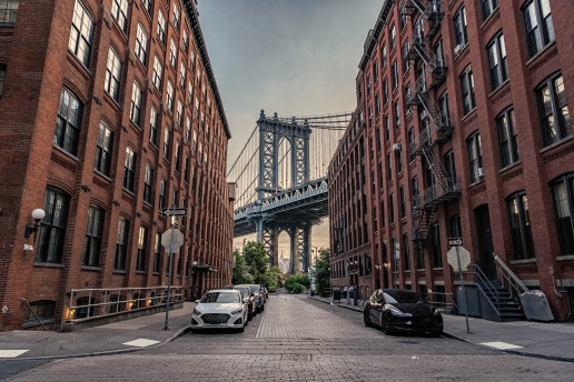 Smalle straat tussen bakstenen pakhuizen met geparkeerde auto's en uitzicht op de Manhattan Bridge in de wijk Dumbo in Brooklyn