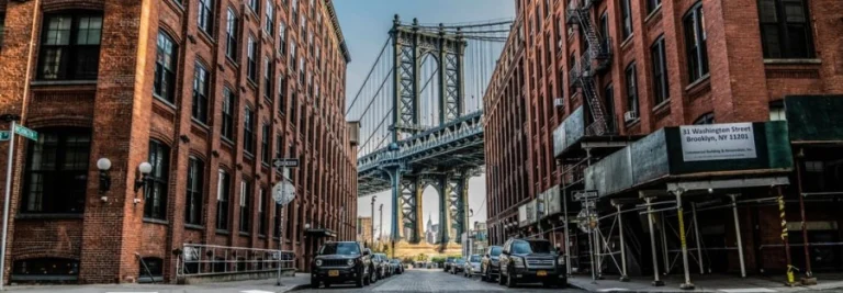 Smalle kasseienstraat tussen bakstenen pakhuizen in Dumbo, Brooklyn met de stalen bogen van de Manhattan Bridge aan het einde van de straat