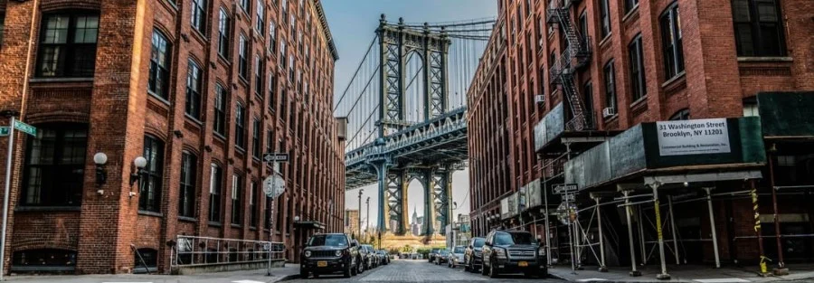 Smalle kasseienstraat tussen bakstenen pakhuizen in Dumbo, Brooklyn met de stalen bogen van de Manhattan Bridge aan het einde van de straat