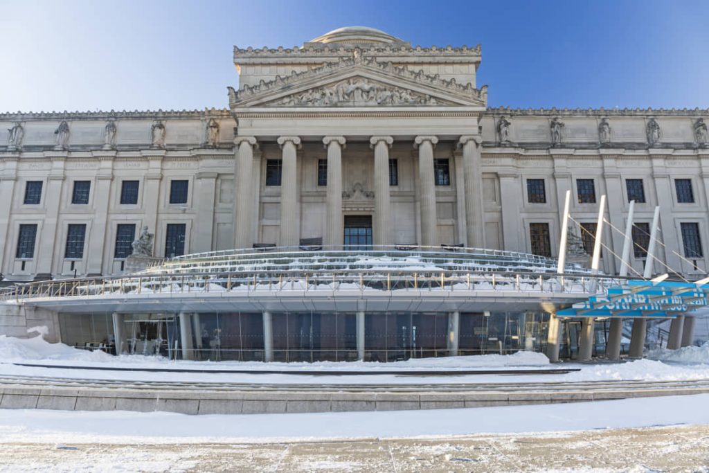 Klassiek zuilenfront van het Brooklyn Museum met een besneeuwd plein en glazen overkapping ervoor