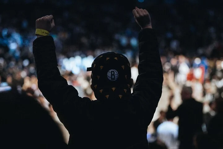 Toeschouwer met een pet van de Brooklyn Nets steekt beide vuisten omhoog terwijl het publiek op de achtergrond juicht