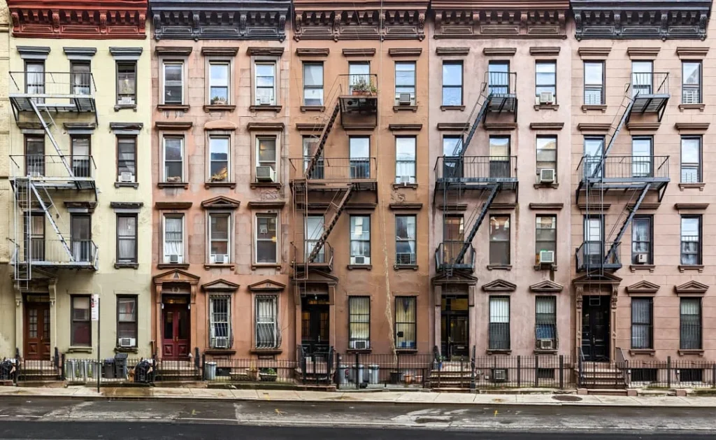 Straat in Brooklyn met een rij vijf verdiepingen tellende appartementengebouwen in geel, roze en bruine tinten met zwarte brandtrappen
