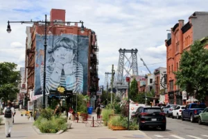 Levendige straat in Williamsburg in Brooklyn met een grote muurschildering van een kind op een gebouw en de Williamsburg Bridge op de achtergrond