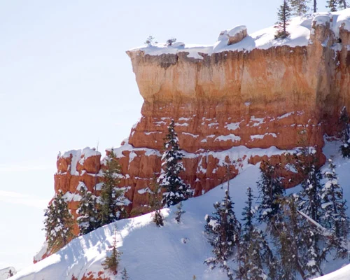 Gelaagde oranje rotswand bedekt met sneeuw en omringd door dennenbomen in Bryce Canyon National Park