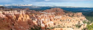 Rossige rotstorens en hoodoos strekken zich uit boven een bebost dal, met heuvels aan de horizon