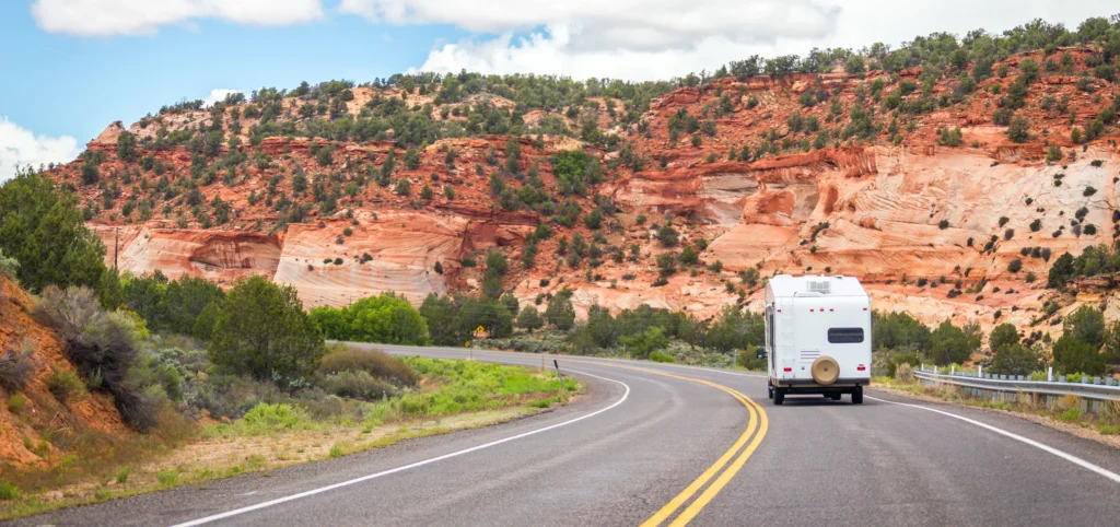 Witte camper rijdt over een weg met haarspeldbocht langs roodoranje rotswanden op weg naar Bryce Canyon in Utah
