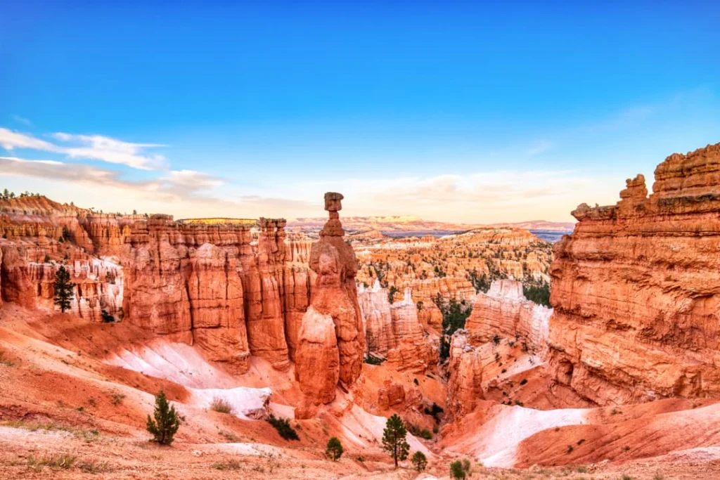 Amfitheater vol oranje en witte rotstorens (hoodoos) van Bryce Canyon onder een blauwe lucht met een enkele wolkenstreep