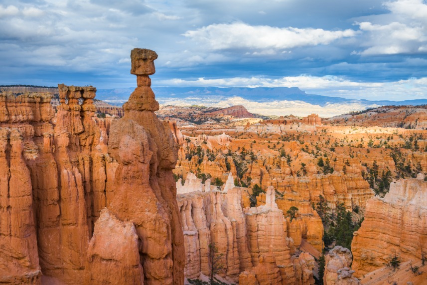 Slanke rotstoren met een plat rotsblok erbovenop, uitkijkend over een uitgestrekt veld van oranje hoodoos in Bryce Canyon