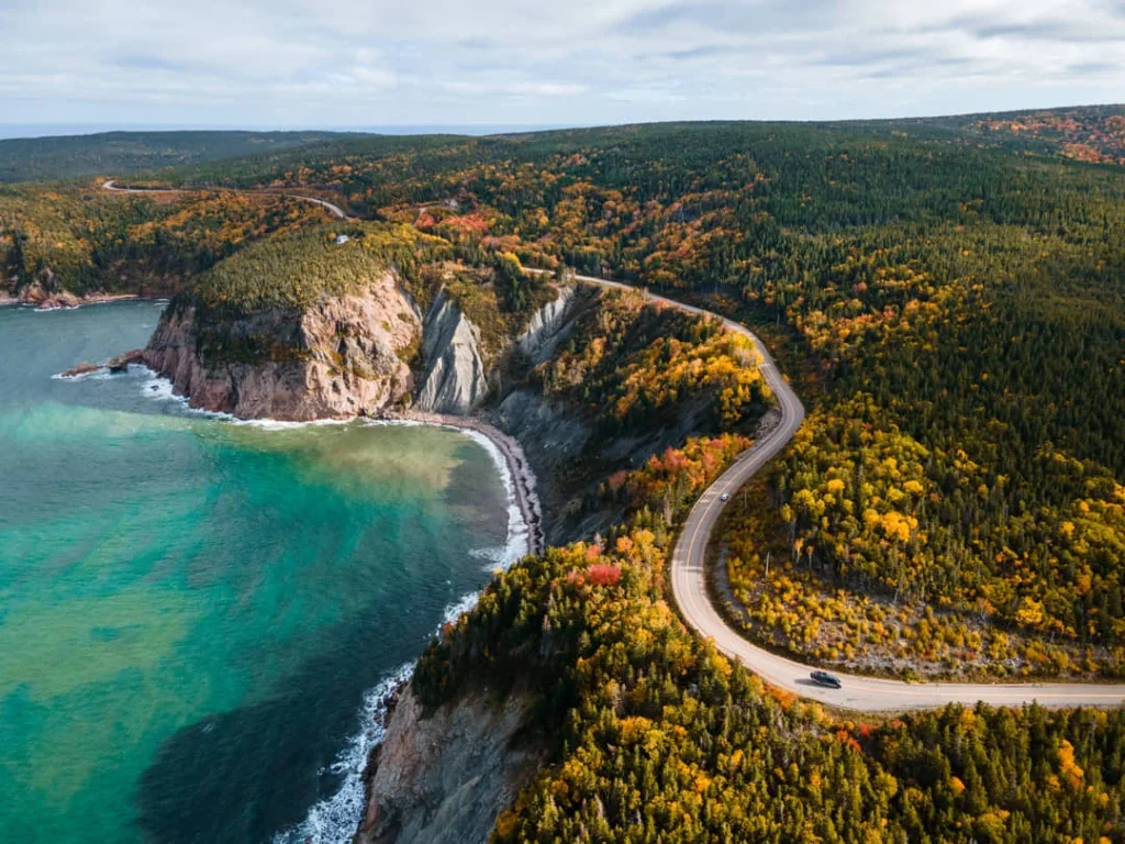 Kustweg de Cabot Trail slingert tussen kliffen en bos in herfstkleuren langs turquoise water op Cape Breton