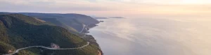Luchtfoto van een kronkelende kustweg die door beboste heuvels loopt langs de oceaan op Cape Breton Island in Nova Scotia bij zonsondergang