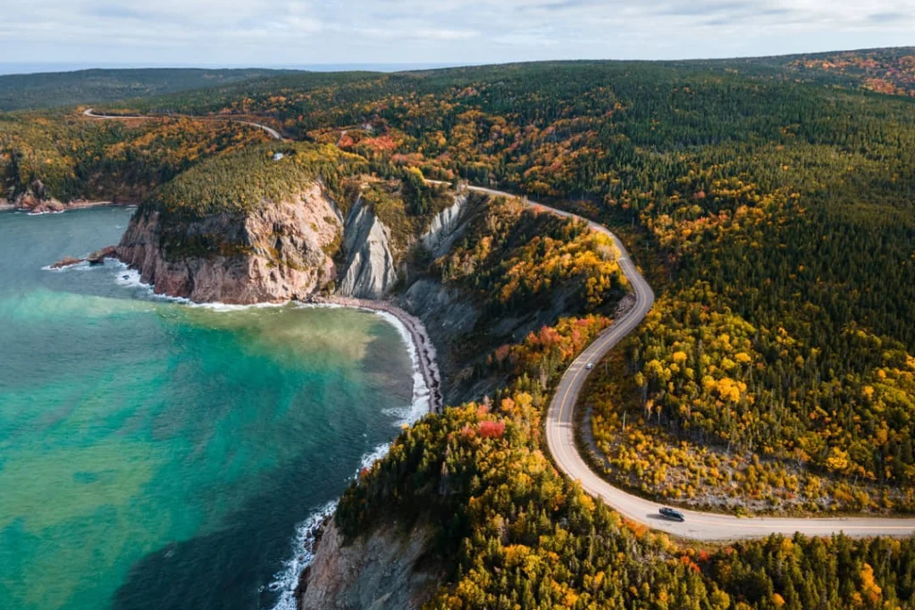 Luchtfoto van een kustweg die tussen rotsachtige kliffen en dicht bos slingert langs turkooisblauw water op Cape Breton Island in Nova Scotia
