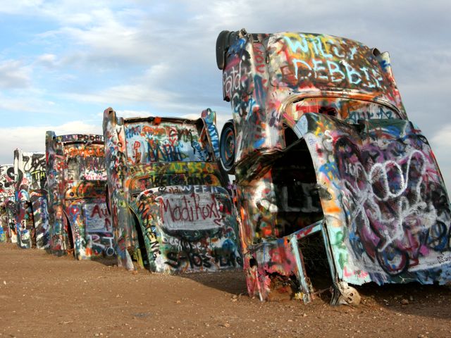 Rij oude Cadillacs half in de grond geplant en volledig bedekt met kleurrijke graffiti bij Cadillac Ranch in Texas