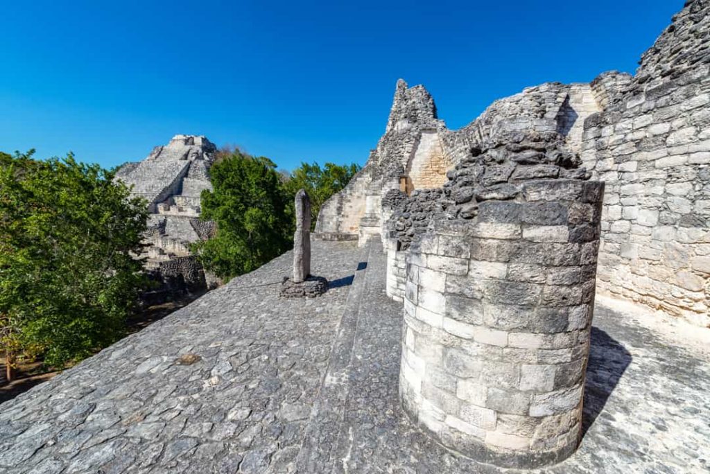 Vanaf de top van een piramide kijk je uit over stenen ruïnes en een tweede piramide boven het jungle bladerdak