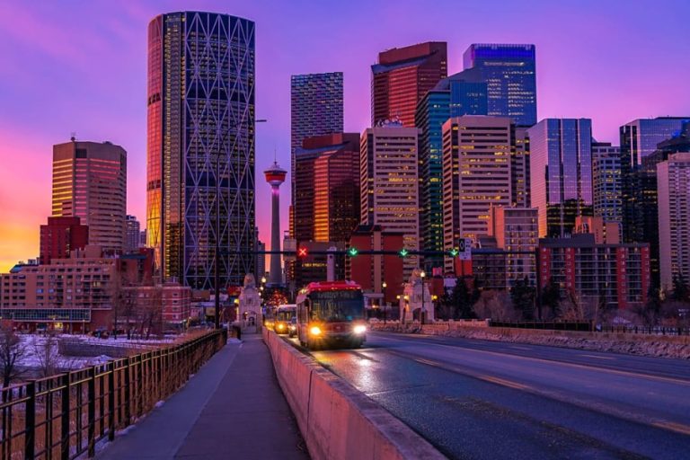 De skyline van Calgary met de Calgary Tower kleurt paars en roze tijdens een levendige zonsondergang terwijl bussen over de brug rijden