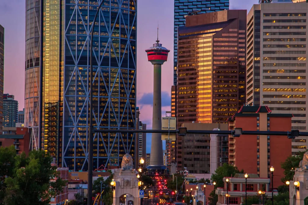 De Calgary Tower rijst op tussen verlichte wolkenkrabbers in het centrum van Calgary tijdens de schemering