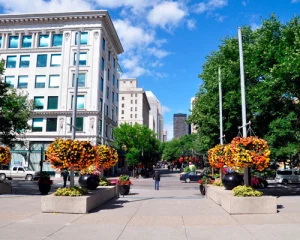 Voetgangersstraat in het centrum van Calgary met historische gebouwen, grote hangende bloemenmanden in oranje en geel en wolkenkrabbers op de achtergrond