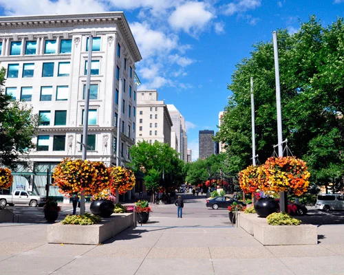 Voetgangersstraat in het centrum van Calgary met historische gebouwen, grote hangende bloemenmanden in oranje en geel en wolkenkrabbers op de achtergrond