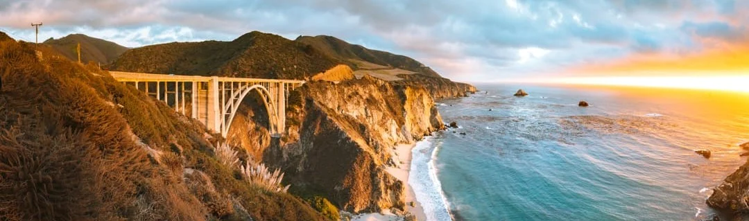 De iconische Bixby Bridge overspant een diep ravijn langs de kustlijn van Californië tijdens een gouden zonsondergang
