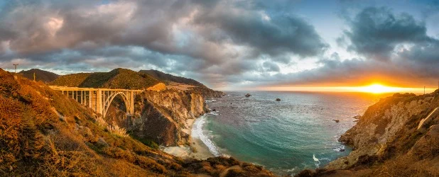 Een boogbrug overspant een rotsachtige kustlijn in Californië terwijl de zon onderdergaat boven de oceaan