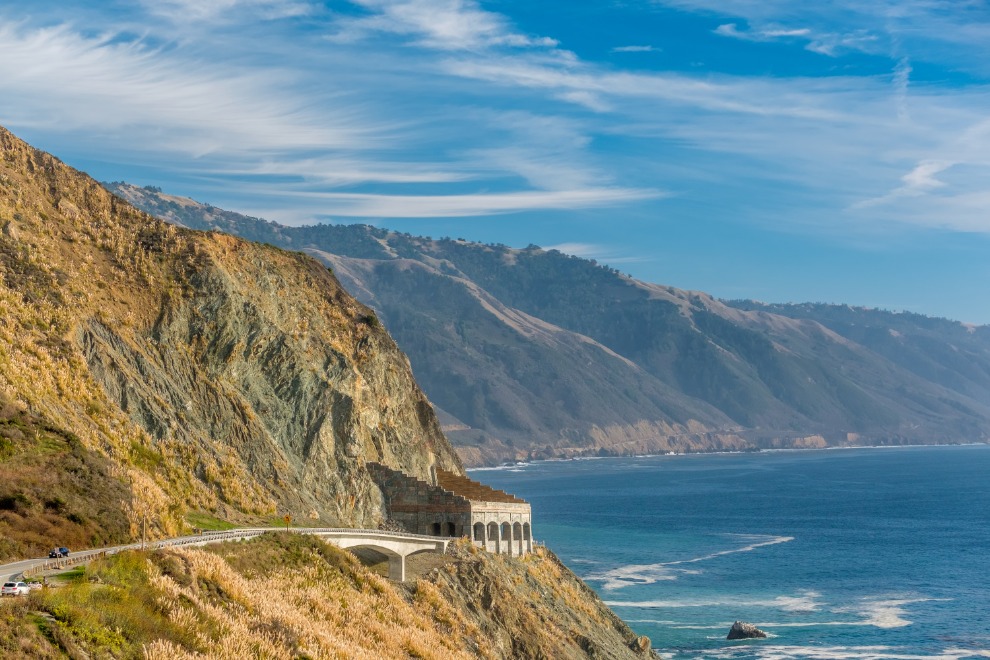 Kronkelende kustweg met brug over een ravijn langs steile groene klippen aan de Pacifische kust in Californië