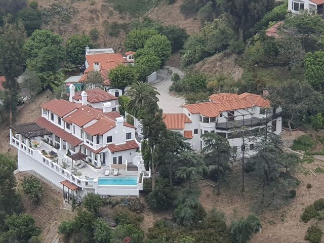 Luchtfoto van een witte villa met rode dakpannen en zwembad tussen groene heuvels in Californië
