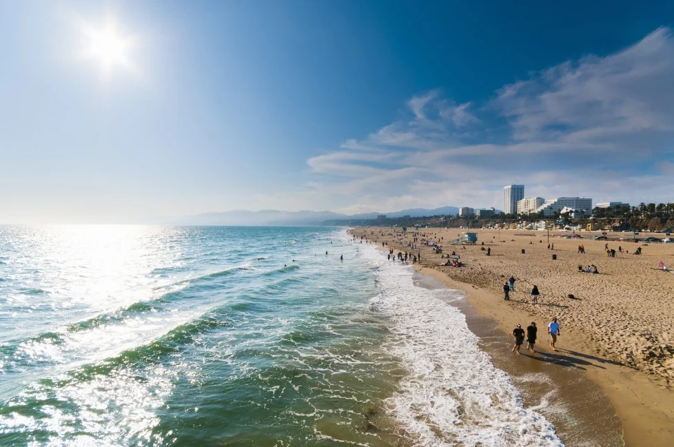 Zonovergoten strand in Californië met wandelaars langs de kust en de skyline van Santa Monica op de achtergrond richting Malibu