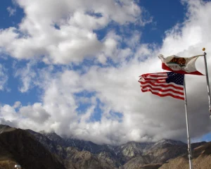 Amerikaanse vlag en de vlag van Californië wapperen in de wind tegen een blauwe lucht met bergen op de achtergrond