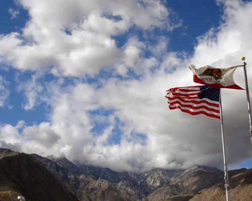 Amerikaanse vlag en de vlag van Californië wapperen in de wind tegen een blauwe lucht met bergen op de achtergrond