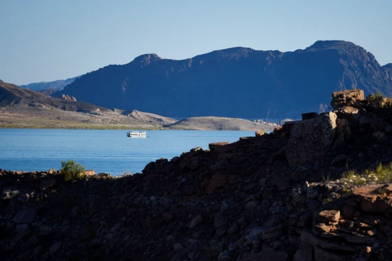 Klein wit bootje vaart over het rustige water van Callville Bay bij Lake Mead met donkere bergen op de achtergrond in de schemering