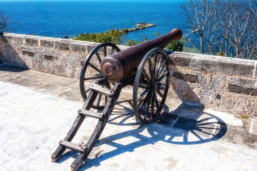 Een roestig historisch kanon op houten wielen staat op een muur met uitzicht over de blauwe zee bij Campeche