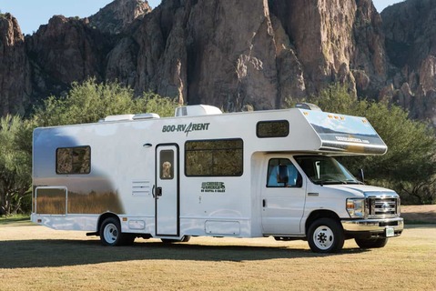 Witte camper met het opschrift 800 RV Rent geparkeerd op droog gras met kartelige rotsachtige bergen op de achtergrond