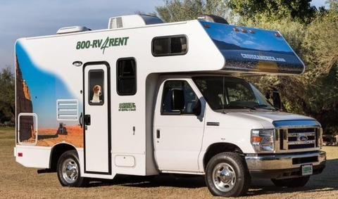 Witte camper met een grote foto van een hond op de zijkant, geparkeerd op een grasveld tussen bomen