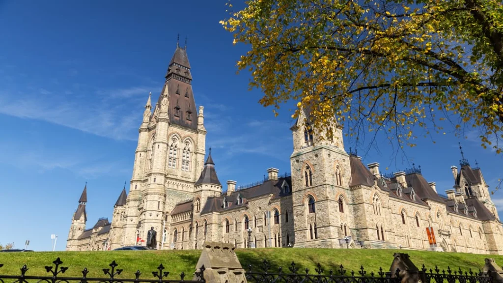 Neogotisch parlementsgebouw met hoge klokkentoren in Canada, met een boom met geel herfstblad op de voorgrond
