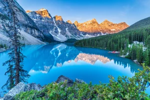 Een turkooisblauw bergmeer in Canada weerspiegelt de besneeuwde bergtoppen en dennenbossen tijdens zonsopgang