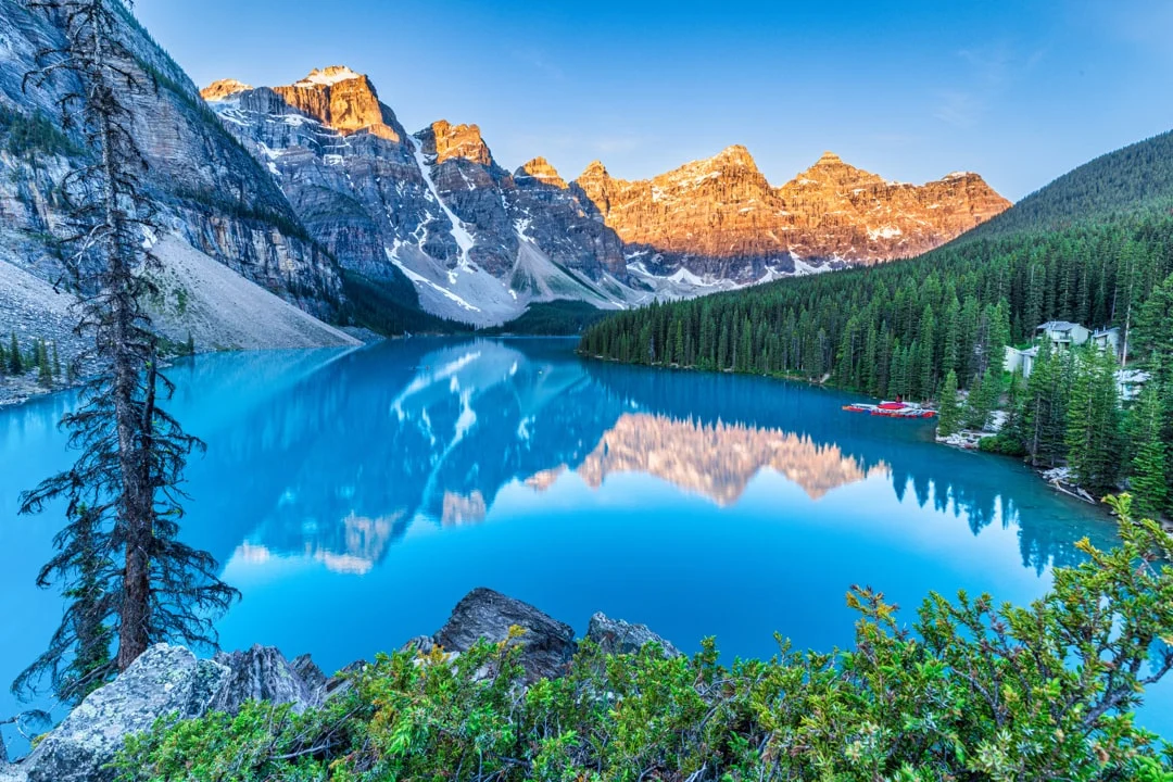 Een turkooisblauw bergmeer in Canada weerspiegelt de besneeuwde bergtoppen en dennenbossen tijdens zonsopgang