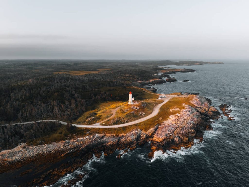Luchtfoto van een witte vuurtoren op een rotsachtig schiereiland aan de ruige kust van Canada