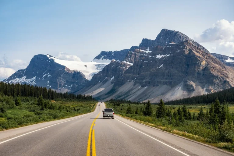 Auto's rijden over een lege snelweg door een vallei met besneeuwde bergtoppen in Banff National Park, Alberta